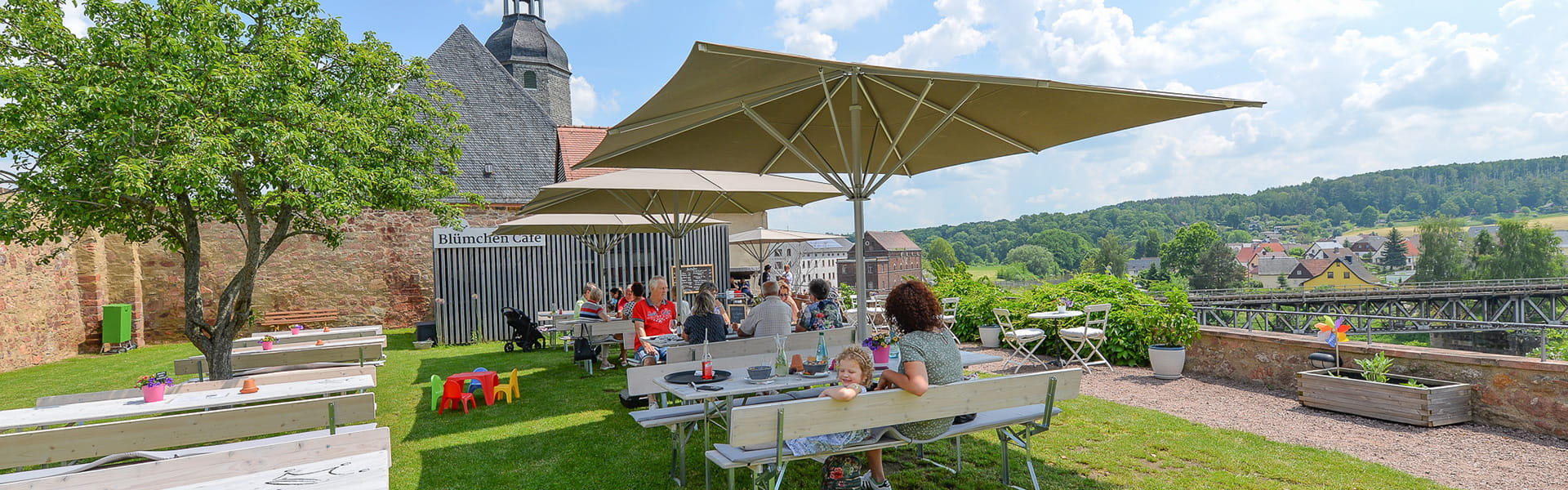 Blümchen Café Rochlitz Blick auf Terrasse mit Gästen unter Sonnenschirmen bei schönem Sommerwetter