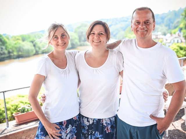 Blümchen Café Rochlitz Team Therés Meier, Sarah Kroth & Frederik Hendler lächeln in die Kamera mit Zwickauer Mulde im Hintergrund bei Sonnenschein