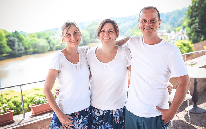 Blümchen Café Rochlitz Team Therés Meier, Sarah Kroth & Frederik Hendler lächeln in die Kamera mit Zwickauer Mulde im Hintergrund bei Sonnenschein