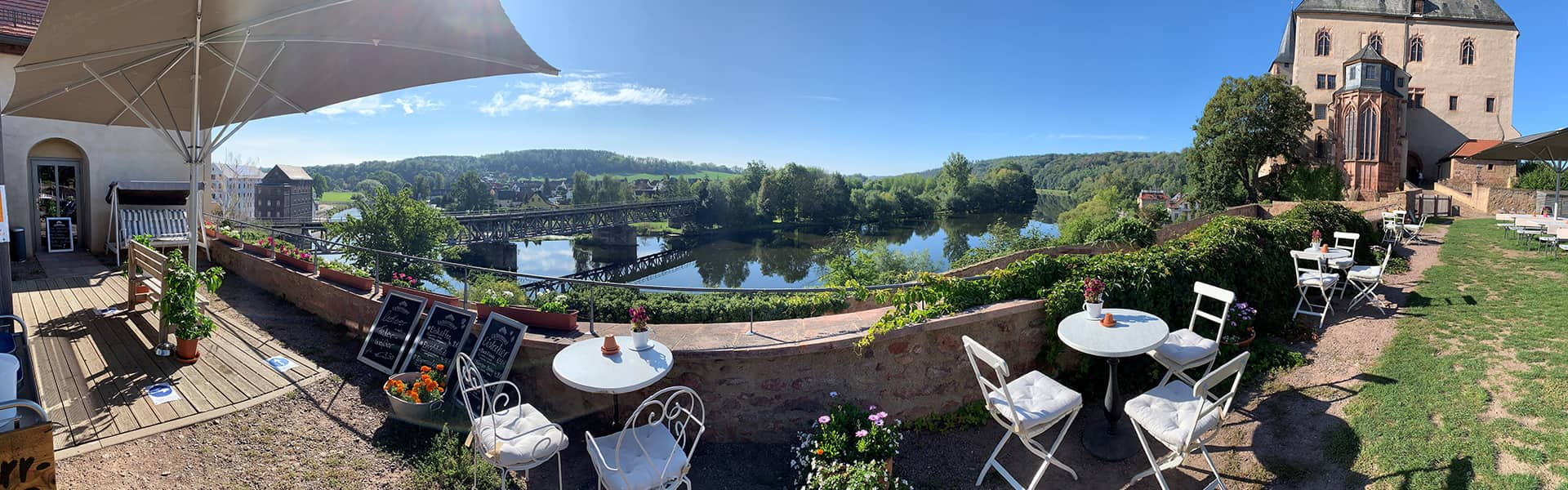 Blümchen Café Rochlitz Panorama Außenbereich mit Blick auf Zwickauer Mulde und Schloss Rochlitz bei Sonnenschein und blauem Himmel