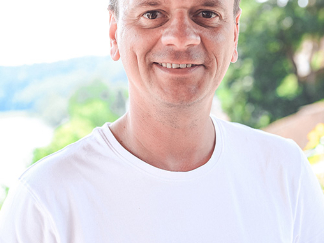 Blümchen Café Rochlitz Frederik Hendler mit weißem T-Shirt lacht in die Kamera mit Zwickauer Mulde im Hintergrund bei Sonnenschein