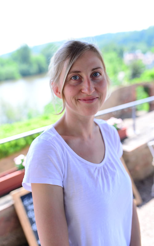 Blümchen Café Rochlitz Therés Meier mit weißem T-Shirt lacht in die Kamera mit Zwickauer Mulde im Hintergrund bei Sonnenschein